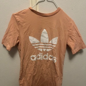 T-shirt från Adidas - Säljer en fin persikofärgad t-shirt från Adidas bra skick Den har en stor vit logga på framsidan och är kortärmad. Jag har inte knappt använt den och den är köpt på jeansbolaget.