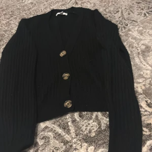 Svart ribbad kofta från H&M - Snygg svart ribbad kofta från H&M med tre knappar framtill. Perfekt för lager-på-lager och att hålla sig varm under kyliga dagar.