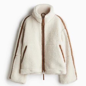 NY Vit teddyjacka med bruna detaljer storlek XS - Ny och oanvänd med prislapp på. Mysig cremevit teddyjacka med bruna detaljer. Jackan har en hög krage och långa ärmar, perfekt för kyliga dagar då den är tjock och lätt vadderad. Storlek XS (oversize) Från H&M. Pilejacka HM. Egna bilder kommer snart! 