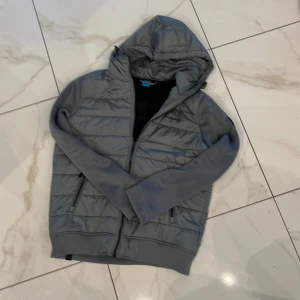 Rökgrå quiltad jacka från Ragwear - Säljer en snygg grå quiltad jacka från Ragwear. Den har en mysig huva och dragkedja framtill. Perfekt för höst och vår med sin stilrena design och bekväma passform. Jackan är i mycket bra skick och redo för nya äventyr!