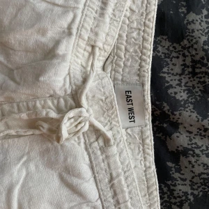 Vita linnebyxor från East West - Säljer ett par vita linnebyxor från East West. De har en avslappnad passform med elastisk midja och snörning för extra komfort. Perfekta för varma sommardagar eller en avslappnad dag hemma. Byxorna har fickor fram och är i ett lätt och luftigt material.