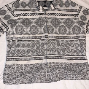 Mönstrad skjorta från Zara - Säljer en unik mönstrad skjorta från Zara i svart och vit. Skjortan har ett coolt geometriskt mönster och, perfekt för sommaren. Den är i bra skick och passar både till vardags och fest. Tillverkad i Marocko.