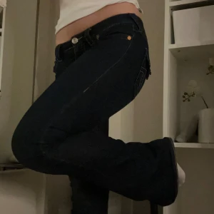 Mörkblå jeans från True Religion - Säljer ett par snygga mörkblå jeans från True Religion. De har en klassisk femficksdesign med en cool knappdetalj på bakfickan. Jeansen är i bootcut-stil och passar perfekt för både vardag och fest. Superbekväma och stilrena! Dom har skavander då jag trampat på dom men annars väldigt fina!!!❤️❤️