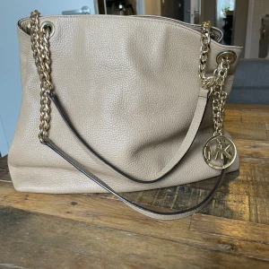 Beige axelväska från Michael Kors - Säljer en snygg beige axelväska från Michael Kors i mycket bra skick. Väskan har en kedjedetalj och en praktisk dragkedja. Perfekt för både vardag och fest! 👜✨B 32cm H 28 cm.