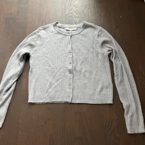 Grå ribbad kofta - Säljer en stilren grå ribbad kofta i mycket bra skick. Den har långa ärmar och knappar framtill, perfekt för lager-på-lager under höst och vår. Supermjuk och bekväm att ha på sig!