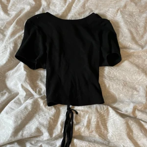 Svart ribbad topp med snörning - Säljer en svart ribbad topp med korta ärmar och snygg snörning i ryggen. Perfekt för en utekväll eller fest! Toppen är croppad och ger en trendig look. Passar bra till både jeans och kjol.