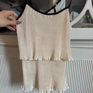 Beige plisserad linne - Säljer ett supergulligt beige linne med plisserad design och svarta axelband. Perfekt för sommardagar eller en avslappnad fest. Den har en luftig passform och volangdetaljer som ger en söt touch. Passar perfekt till jeans eller kjol!