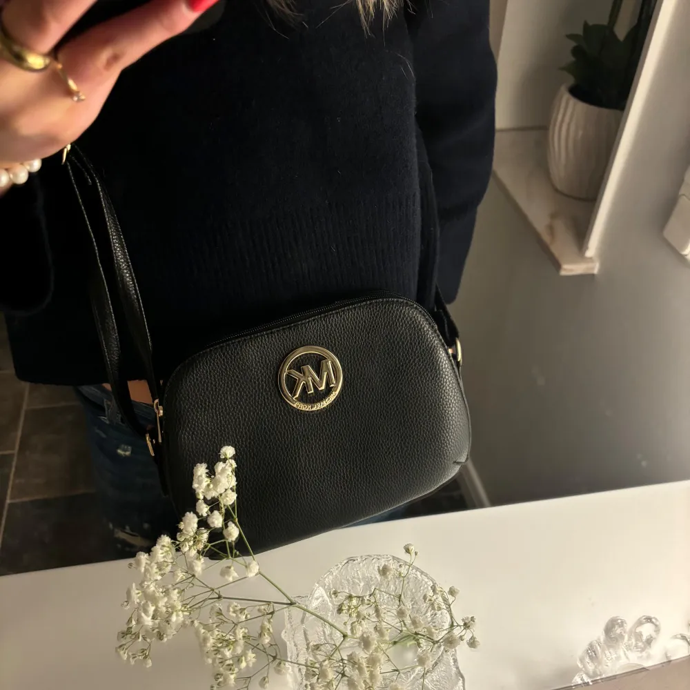 Snygg svart axelväska i skinn med gulddetaljer och Michael Kors logotyp framtill. Perfekt för både vardag och fest. Väskan har en justerbar rem och en praktisk dragkedja för säker förvaring. En stilren accessoar som passar till alla outfits särskilt nu till höst och vintern💕(obs inte äkta). Väskor.