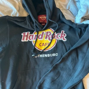 Svart hoodie från Hard Rock Cafe strl M - Säljer en svart hoodie från Hard Rock Cafe med Göteborg-tryck. Den är superbekväm och perfekt för en avslappnad stil. Har en klassisk känguruficka och justerbar huva. Perfekt för höst och vinter!