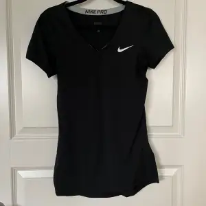 Säljer en svart Nike Pro träningstopp i storlek S. Toppen har en v-ringad design och korta ärmar, perfekt för träning. Den är i mycket bra skick och har den klassiska Nike-loggan på bröstet. Perfekt för gymmet eller löprundan!