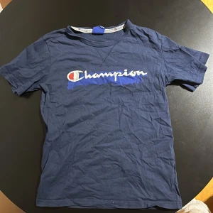 Blå t-shirt från Champion - Säljer en blå t-shirt från Champion i bra skick. Den har korta ärmar och det klassiska Champion-loggan tryckt på framsidan. Perfekt för vardagsbruk eller träning. Skön och enkel stil som passar till det mesta. Hör av dig vid intresse!