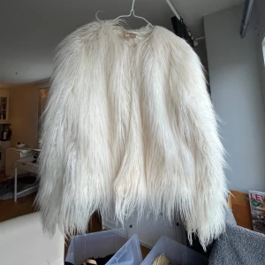 Fuskpäls från H&M i nyskick  - Vit fluffig jacka i fuskpäls från H&M.  Jackan har en enkel design med en rund halsringning och inga fickor. Den är perfekt för att addera en touch av lyx till din vintergarderob.   Längd: Midjelång  Storlek: 36  Absolut nyskick.