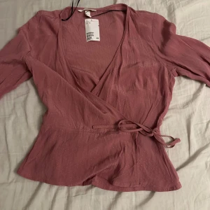 Rosa omlottopp med knytband - Säljer en superfin rosa omlottopp från H&M i storlek S. Toppen har långa ärmar och ett knytband i midjan för en snygg passform. Perfekt för både vardag och fest! 💖