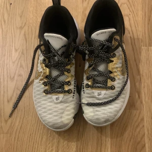 Nike Giannis Antetokounmpo sneakers - Säljer ett par Nike Giannis Antetokounmpo sneakers i mycket bra skick. Skorna är vita med guldiga detaljer och har en snygg svart sula. De har snörning och är perfekta för både träning och vardag. Storlek dam 38.