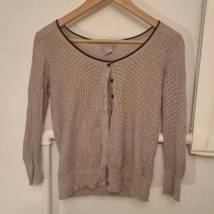Beige stickad kofta - Säljer en beige stickad kofta med knappar framtill. Den har en ribbad kant och trekvartsärmar. Koftan är i mycket bra skick och är i strl M men skulle säga att den passar S ungefär 