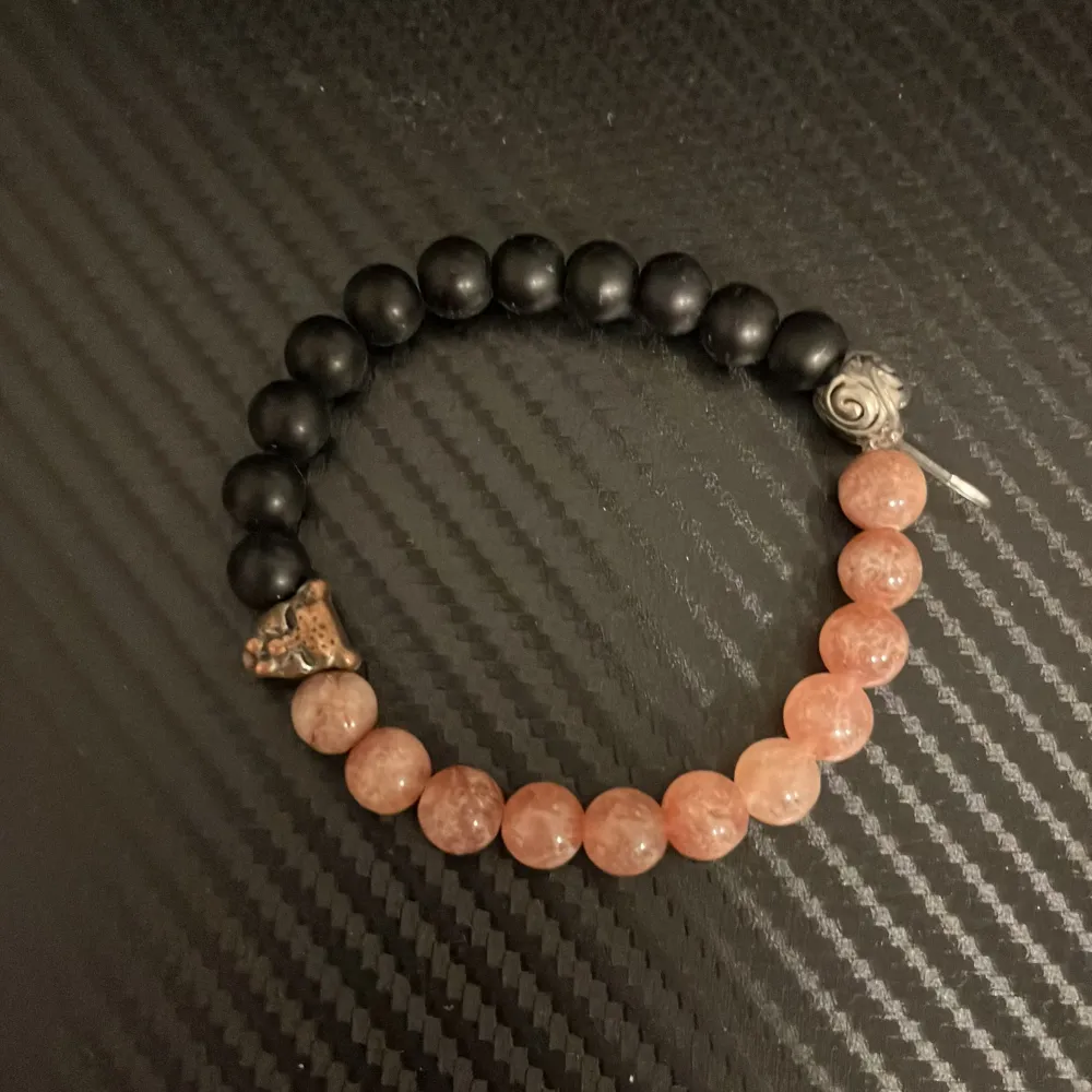 Snyggt armband med svarta och rosa pärlor. Armbandet har en cool detalj i form av ett litet lejonhuvud i metall. Perfekt accessoar för att ge din outfit en unik touch. Passar både till vardags och fest!. Accessoarer.