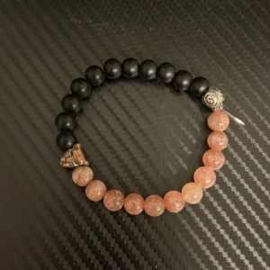 Svart och rosa armband med pärlor - Snyggt armband med svarta och rosa pärlor. Armbandet har en cool detalj i form av ett litet lejonhuvud i metall. Perfekt accessoar för att ge din outfit en unik touch. Passar både till vardags och fest!