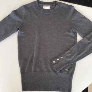 Grå stickad tröja med guld detaljer  - Grå stickad tröja med guldiga detaljer på armarna. Från Lindex/ Holly and white i storlek XS. En liten guld detalj har går av lite men det går att du tillbaka. 