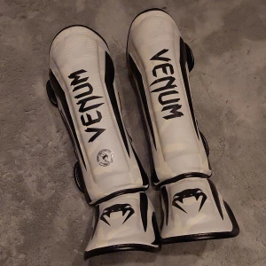 Venum chin guards Elite - Oanvända Venum Elite benskydd - i snyggaste färgen Vit/Camo. Superbra märke, välgjorda, skaver ej, sitter bra. Googla för produktinfo. Ordinarie pris på venum idag 109,99 €. Inköpta från Venum, finns kvitto.   Strl L. 