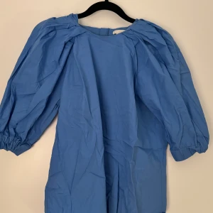 Blå klänning med puffärmar - Säljer en superfin blå blus med puffiga trekvartsärmar. Den har en dragkedja i ryggen som gör den lätt att ta på och av. Perfekt för både vardag och festliga tillfällen!
