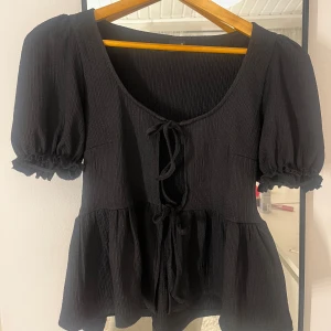 Svart ribbad topp med knytning - Säljer en superfin svart ribbad topp med korta puffärmar och knytning framtill🤩från ginatricot endast använd en gång