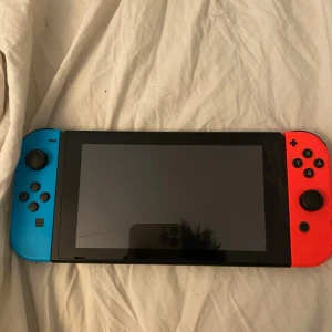 Nintendo Switch med blå och röd Joy-Con - Säljer en Nintendo Switch med neonblå och neonröd Joy-Con. Konsolen är i bra skick och fungerar perfekt för både handhållet och dockat spelande. Perfekt för att spela dina favoritspel hemma eller på resande fot. Perfekt för gamingkvällar med vänner! 🎮