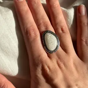 Säljer en superfin ring med en stor vit sten i mitten. Ringen har en elegant silverfärgad ram med detaljer som ger den en vintagekänsla. Perfekt för att piffa upp vilken outfit som helst, oavsett om det är till vardags eller fest. Passar de flesta storlekar eftersom den är justerbar.