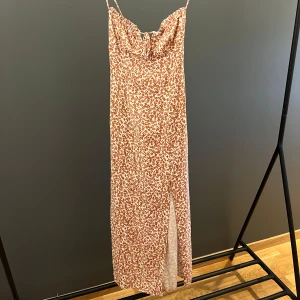 Klänning - Blommig klänning med smala band, knytning framtill och en dragkedja vid sidan. Klänningen har även en slits nedtill och kommer ifrån Pull&Bear. Använd få gånger så i fint skick, Storlek XS🩷