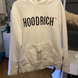 Säljer en snygg vit hoodie från Hoodrich i storlek M. Den har en stor ficka fram och texten 'HOODRICH' tryckt både fram och bak. Perfekt för en casual look och superbekväm att ha på sig. Passar perfekt till höst och vår!