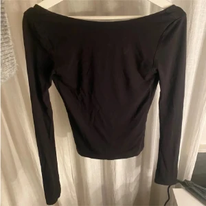 Svart långärmad topp - Snygg svart långärmad topp med hål där bak. Perfekt för en stilren look. Passar bra till allt. Från Gina och Inga defekter alls förutom bortklippt lapp men syns ej när den är på. Sitter som en Xs/XXs. 