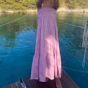 Rosa långklänning zara - Säljer en romantisk rosa axelbandslös långklänning med volanger. Perfekt för somriga dagar vid vattnet. Klänningen har en luftig passform och är gjord i ett lätt material.