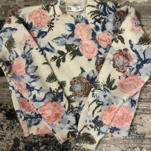 Elegant blommigt tröja från Zara - Säljer en mysig blommig tröja från Zara i mjuka färger. Tröjan har en vit bas med rosa och blå blommor samt gröna blad. Den är långärmad och perfekt för en stilfull och elegant look. Perfekt för vintern. 