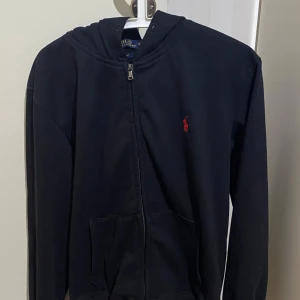  Ralph Lauren zip up  - Snygg svart hoodie från Ralph Lauren med dragkedja och röd broderad logga på bröstet. Perfekt för en casual look. Har inte snöre rund luvan. Priset kan diskuteras.