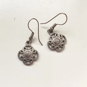 Silverfärgade örhängen med blommönster - Charmiga silverfärgade örhängen med ett detaljerat blommönster. De har en krokdesign som gör dem enkla att bära. Perfekta för att ge en elegant touch till din stil.