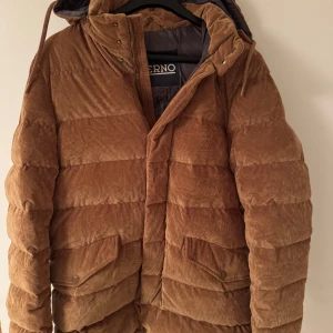 Brun manchesterjacka från Herno - Snygg brun manchesterjacka från Herno med huva och dragkedja. Jackan har en quiltad design och praktiska fickor med knappar. Perfekt för kyligare dagar.