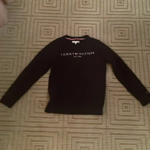 Svart tröja från Tommy Hilfiger - Säljer en stilren svart tröja från Tommy Hilfiger med deras ikoniska logga på bröstet. Tröjan har långa ärmar och ribbade muddar. Perfekt för en casual look.