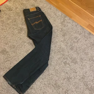 Mörkblå jeans från Nudie Jeans - Snygga mörkblå jeans från Nudie Jeans med klassisk femficksdesign och orange sömmar. Perfekt skick aldrig använda. Hör av er om ni har några frågor. Priset ej hugget i sten!!