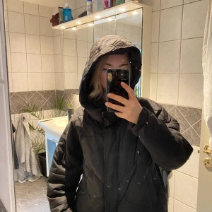 Svart dunjacka med huva - Säljer en svart dunjacka med huva, perfekt för kalla dagar. Jackan har en pufferdesign. Den är idealisk för vinter och höst.