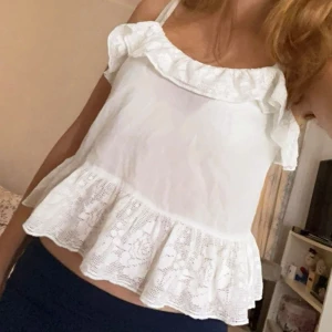 Vit ärmlös topp med volang - Söt vit ärmlös topp med volangdetaljer. Perfekt för sommardagar och kan enkelt matchas med jeans eller kjol. Toppen har en luftig passform och är gjord i ett lätt material.