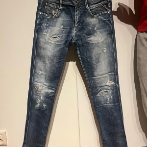 Replay Jeans - Säljer ett par blå jeans med slitningar och en cool, distressed look. De har en klassisk femficksdesign och en snygg tvättad finish. Perfekta för en avslappnad stil.