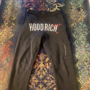 Svarta mjukisbyxor från Hoodrich - Snygga svarta mjukisbyxor från Hoodrich med stort tryck på framsidan. Byxorna har en elastisk midja och en praktisk ficka på sidan. Perfekta för en avslappnad stil.