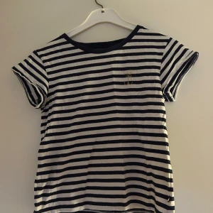 Randig t-shirt med broderad detalj - Snygg randig t-shirt i marinblå och vit med en subtil broderad detalj på bröstet. Perfekt för en avslappnad stil. Kortärmad och bekväm passform.