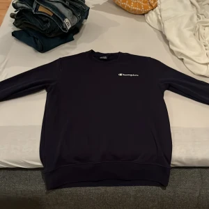 Svart sweatshirt från Champion - Säljer en stilren svart sweatshirt från Champion med deras ikoniska logga på bröstet och ärmen. Perfekt för en avslappnad look. Tröjan har långa ärmar och en bekväm passform.