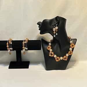 Smyckesset med pärlor och orange detaljer - Elegant smyckesset bestående av halsband, armband och örhängen. Setet har stora vita pärlor och orange glittriga detaljer som ger en lyxig känsla. Perfekt för att lyfta en outfit med sina skimrande och färgglada inslag. Ett par örhängen och ett par armband plus en halsband handgjorda mycket mycket fint nytt oanvänd 