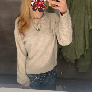 Beige stickad tröja - Säljer en mysig beige stickad tröja med långa ärmar. Perfekt för kyligare dagar och lätt att matcha med olika outfits. Tröjan har en klassisk design med ribbade detaljer vid ärmslut och nederkant.