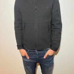 Svart jacka från J.Lindeberg - Snygg svart jacka från J.Lindeberg med dragkedja framtill och praktiska fickor. Perfekt för en stilren look. Tillverkad i ett bekvämt material som passar bra till vardags.