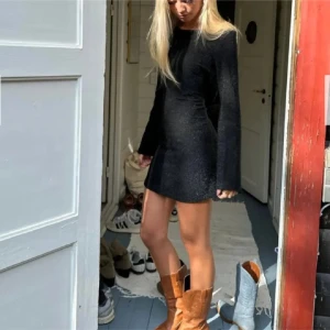 Svart glittrig klänning med öppen rygg - Snygg svart klänning med glittrande detaljer och en öppen rygg med snörning. Klänningen har långa ärmar som är lätt vida ner till, perfekt till nyår, endast använd en gång! Den är i storlek XS/S