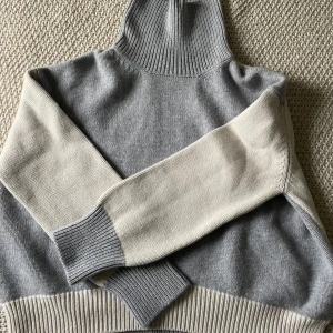 Grå och beige cashmere polotröja från Nathalie Schuterman - Snygg och stilren polotröja i grått och beige från Nathalie Schuterman. Tröjan har en hög ribbad krage och långa ärmar med ribbade muddar. Nypris ca 15 000kr och enbart använd två gånger.