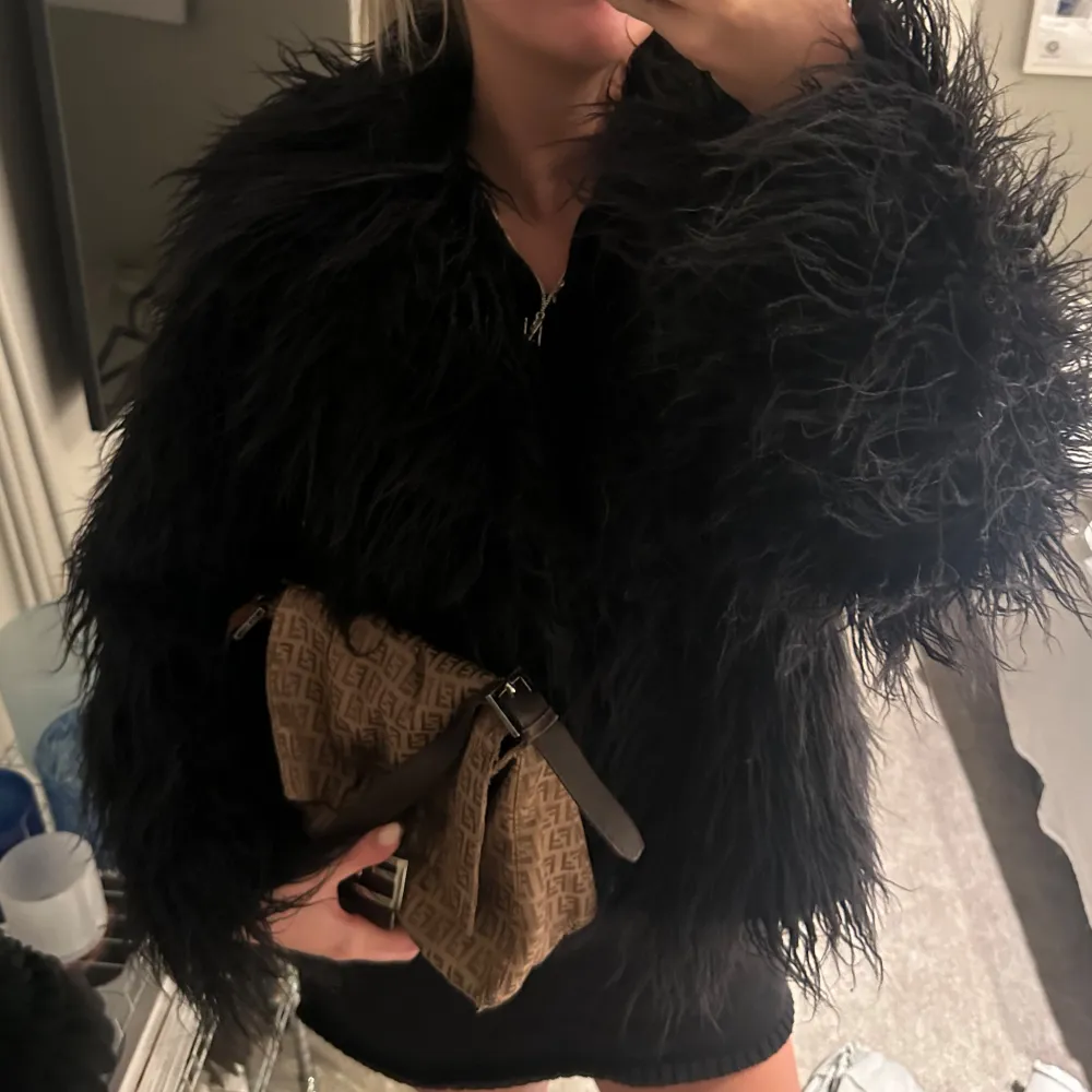 Säljer en svart pälsjacka med långärmad design. Jackan har en fluffig och trendig look. Den är idealisk för kyligare dagar och ger en lyxig känsla. . Takit.