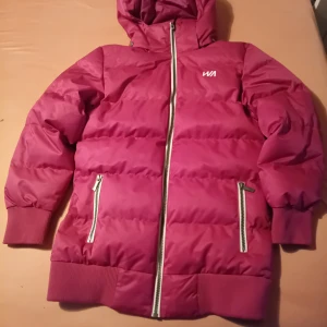 Röd pufferjacka från WA - Säljer en snygg röd pufferjacka från WA med dragkedja och huva. Jackan har ribbade muddar och två praktiska fickor med dragkedjor. Perfekt för kyliga dagar.